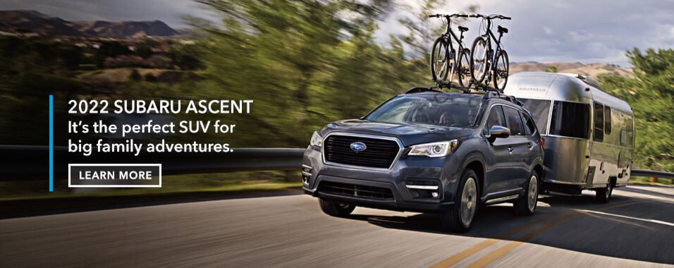 Grey 2022 Subaru Ascent with bicycles on roof rack, towing a family trailer.